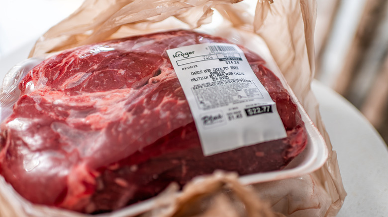Packaged chuck pot roast from Kroger sitting on the counter atop a plastic grocery shopping bag