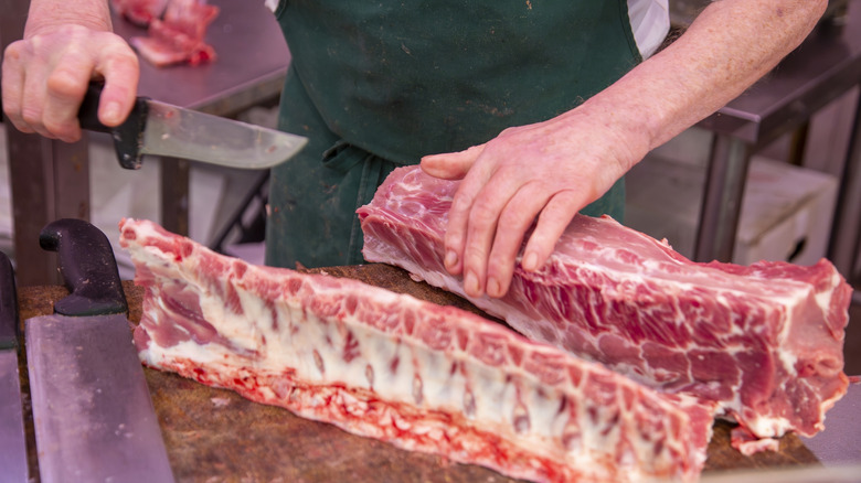 Butcher with dark green apron holding a knife and breaking down a pork carcass