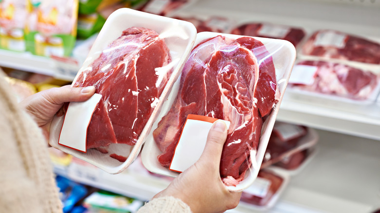 Person in the meat department at the store holding two packages of steak