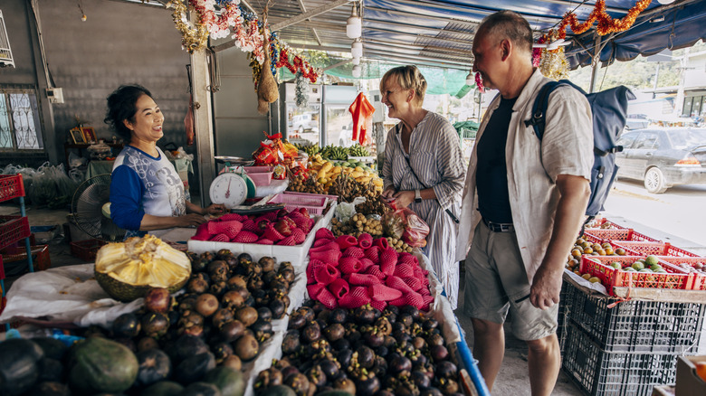 A man and women speak with a women at a fruit stand on the sidewalk