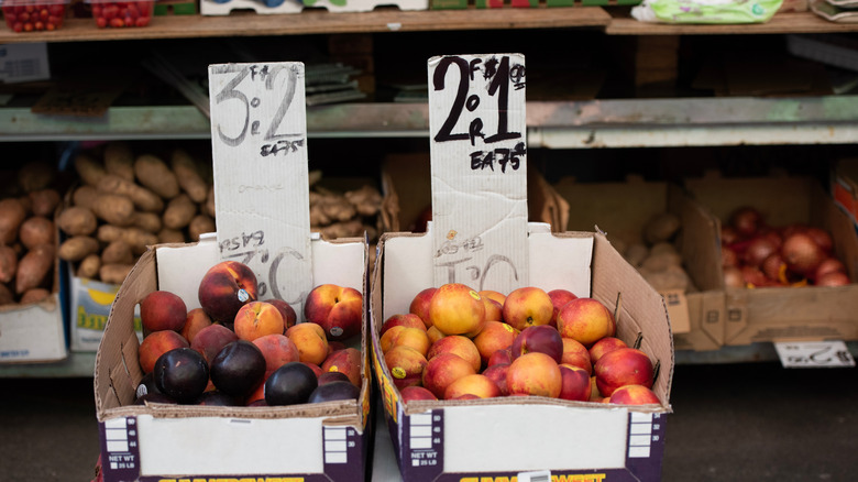 A farmstand selling peaches with potatoes and onions in the background
