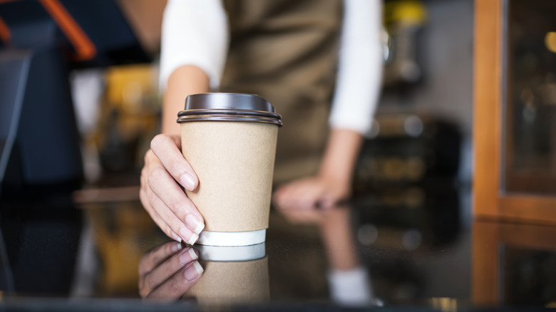 A barista placing a drink in a takeout cup on a table