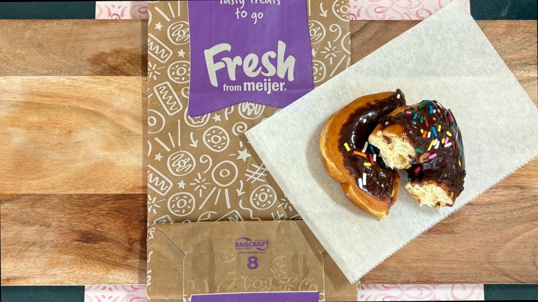 Meijer chocolate iced donut with sprinkles, cut in half on wax paper on top of store bag