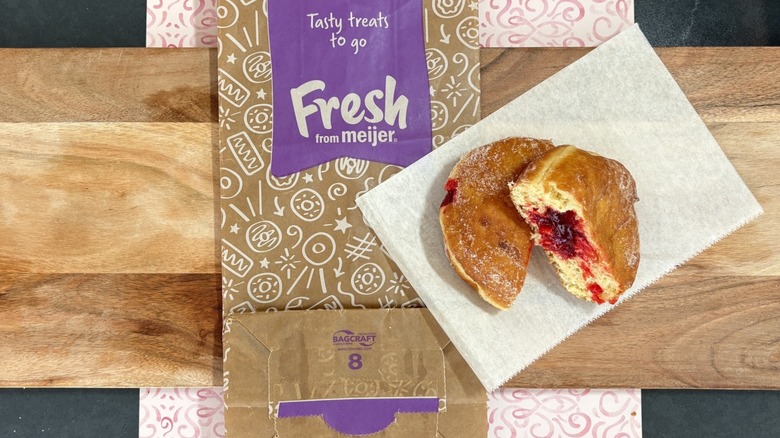 Meijer jelly filled, sugar topped donut cut in half on wax paper on top of store bag and cutting board