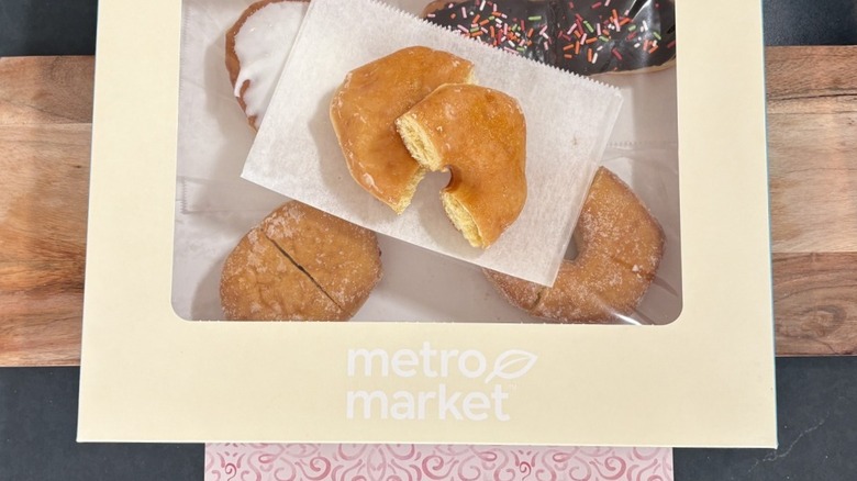 Metro Market glazed donut cut in half on wax paper on top of box of assorted donuts