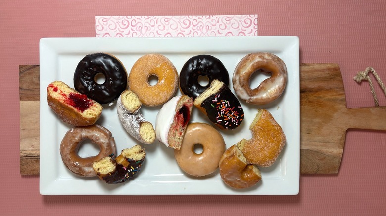 Some whole and some halved donuts on a white serving tray atop a wooden serving board and pink tablecloth