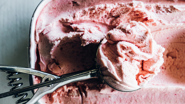 Strawberry ice cream is scooped out of a tub