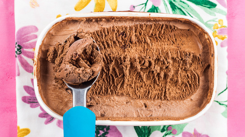 Chocolate ice cream is scooped out of a tub