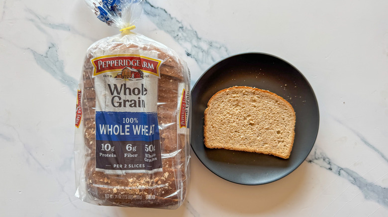 Package of Pepperidge Farm whole wheat bread next to a slice of bread on a black plate on a marble countertop