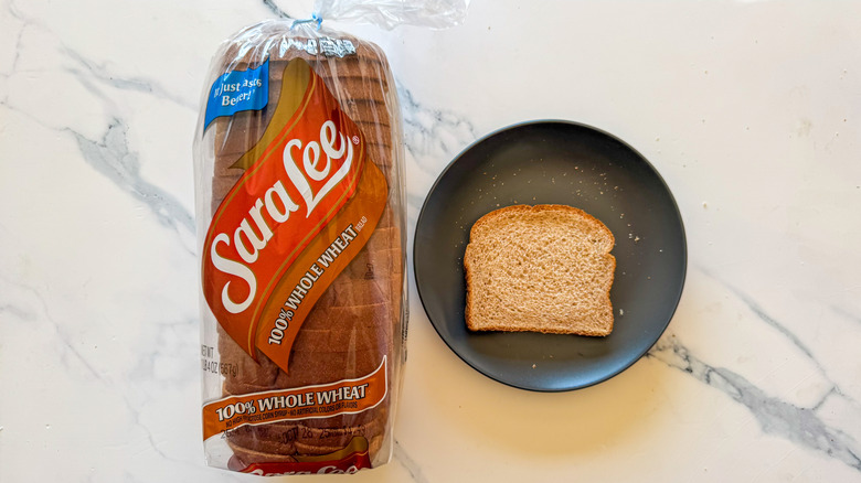 Package of Sara Lee whole wheat bread next to a slice of bread on a black plate on a marble countertop