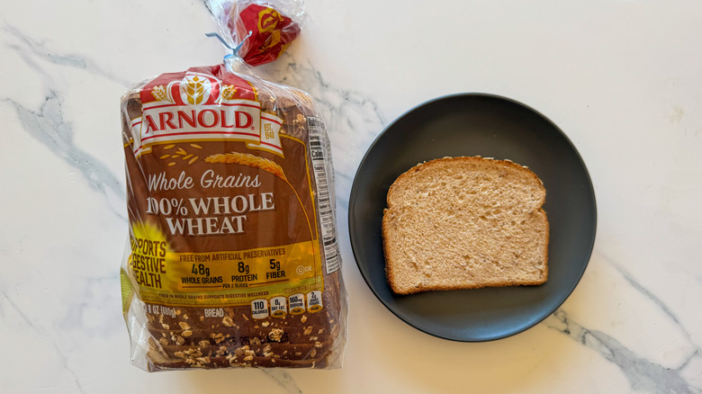 Package of Arnold whole wheat bread next to a slice of bread on a black plate on a marble countertop