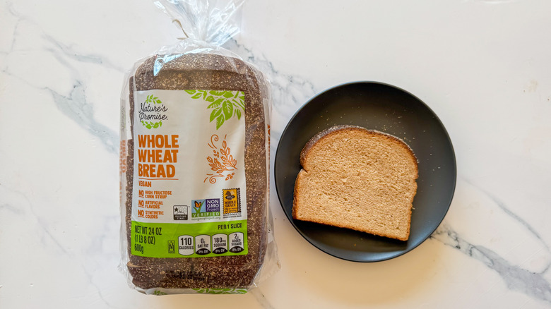 Package of Nature's Promise whole wheat bread next to a slice of bread on a black plate on a marble countertop