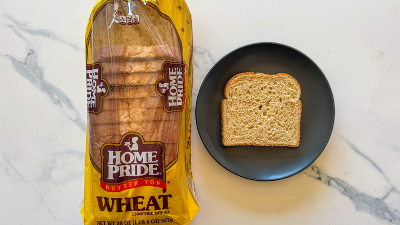 Package of Home Pride butter top whole wheat bread next to a slice of bread on a black plate on a marble countertop