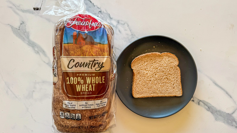 Package of Freihofer's whole wheat bread next to a slice of bread on a black plate on a marble countertop