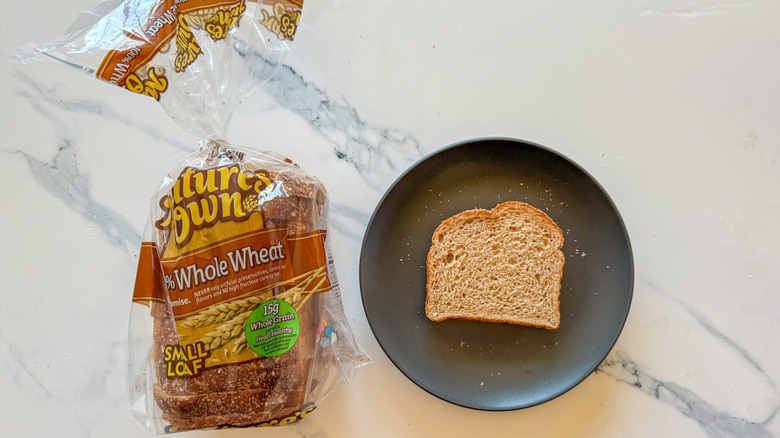 Package of Nature's Own whole wheat bread next to a slice of bread on a black plate on a marble countertop
