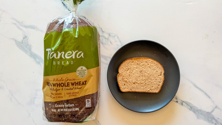 Package of Panera whole wheat bread next to a slice of bread on a black plate on a marble countertop