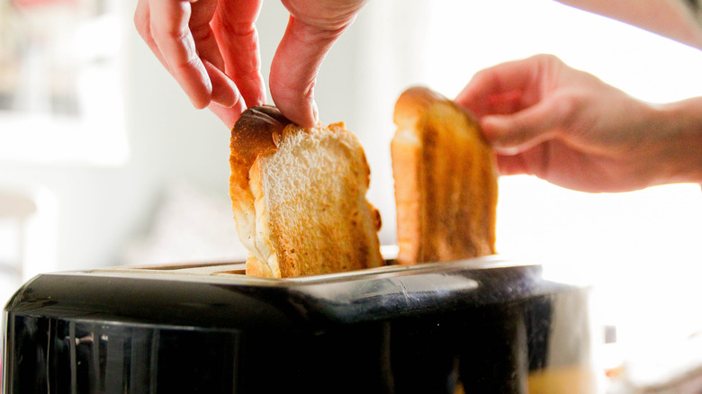 Two hands lifting two slices of toast out of a toaster