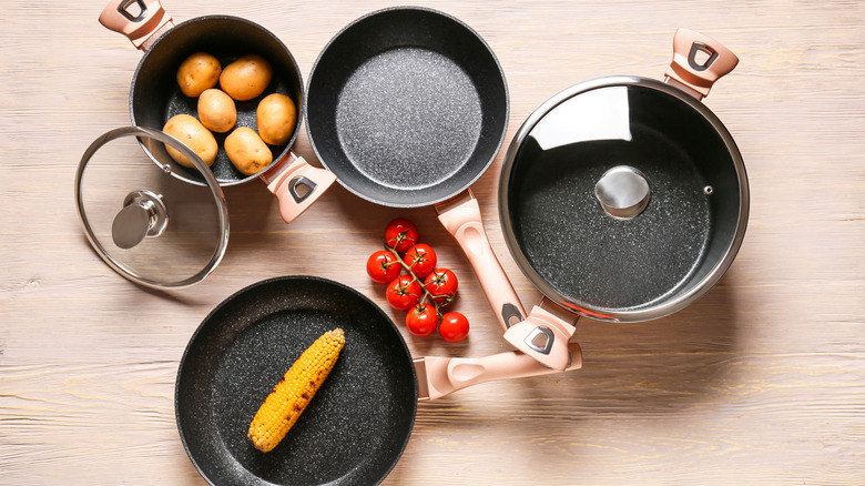 Bird's-eye view of several cooking pans with corn on the cob, tomatoes, and potatoes inside