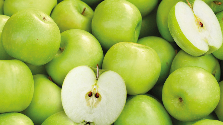 A pile of Granny Smith apples, with some whole and two halves