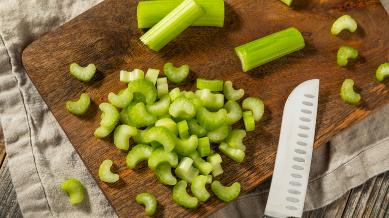 Celery slices and sticks next to a santoku knife on a wooden cutting board