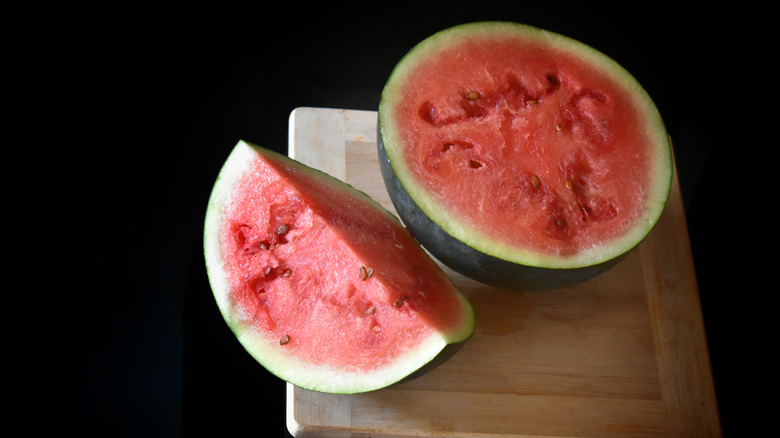 One half and one quarter of a watermelon on a wooden cutting board