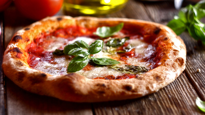A neapolitan pizza with charred edges topped with tomato, mozzarella cheese, and basil