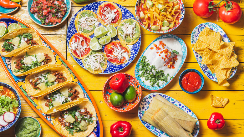 A table filled with various Mexican dishes, including tacos, guacamole, picadas, chiles en nogada, and salsa