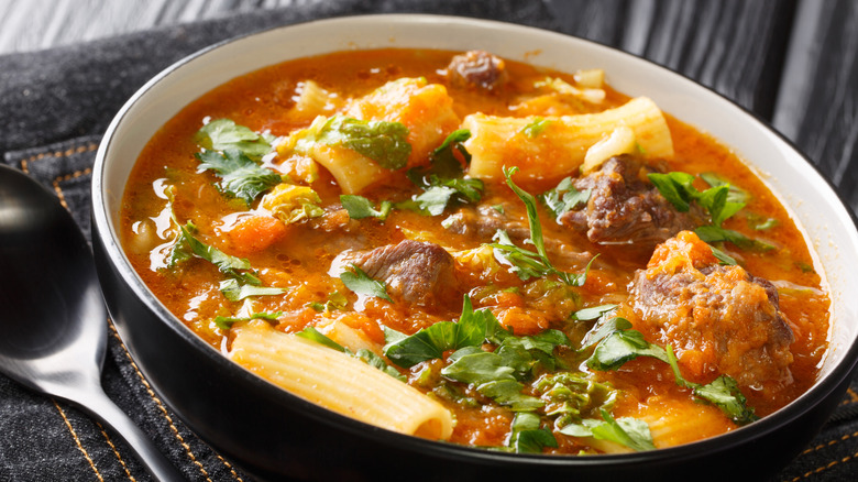 A bowl of joumou soup featuring pumpkin, root vegetables, beans, meat, and herbs