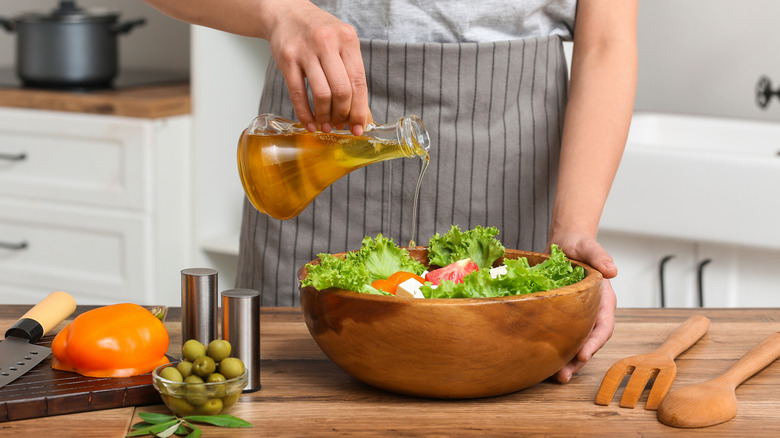 A person pouring olive oil onto a salad in a wooden bowl