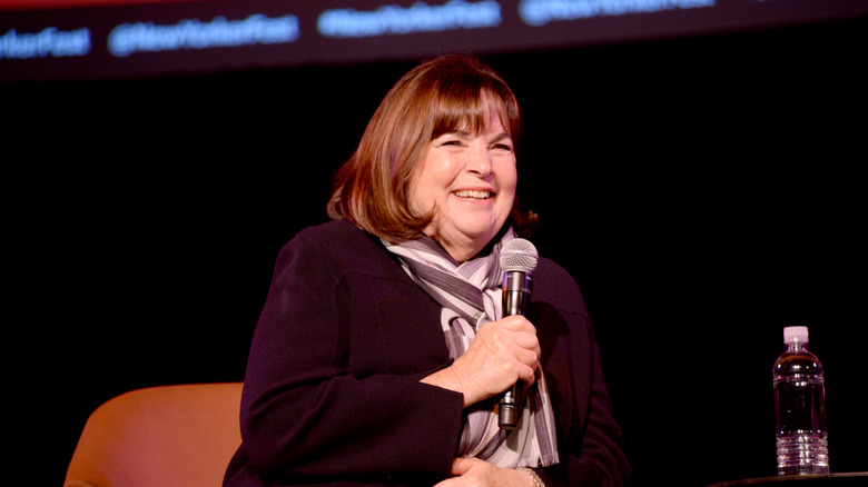 Ina Garten smiling and speaking on stage with a microphone in hand