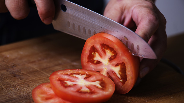 A person slicing a large tomato with a chef's knife