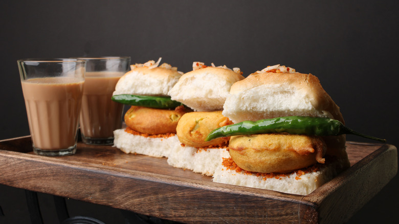 Three vada pav sandwiches with chai tea on a wooden tray