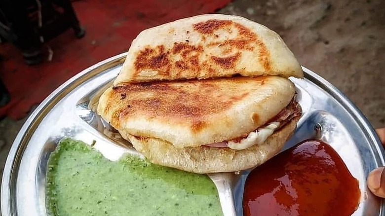 A kaladi kulcha sandwich on a plate with condiments