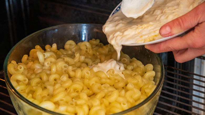 hands adding creamy liquid to a bowl of macaroni