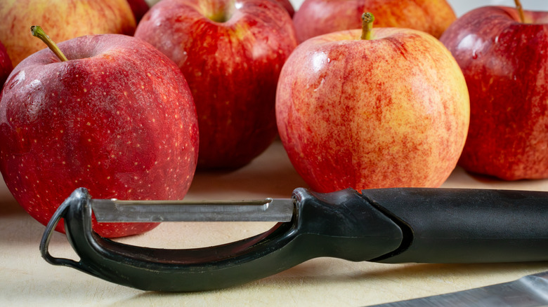 A vegetable peeler lays in front of several red apples