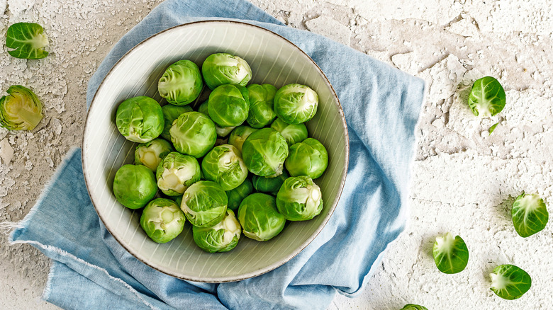 Brussels sprouts in a bowl on a rocky surface, with some scattered across the surface.