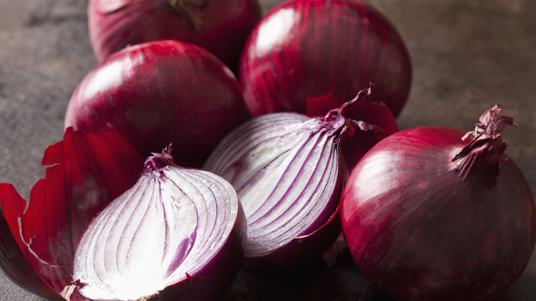 Red onions, some whole and some cut crosswise, on a dark, earthy background.
