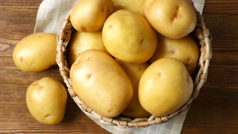 Young yellow potatoes in a basket atop a wooden table set with a cloth.