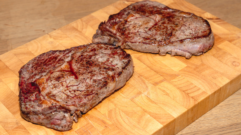 Cooked ribeye steaks resting on wooden slab