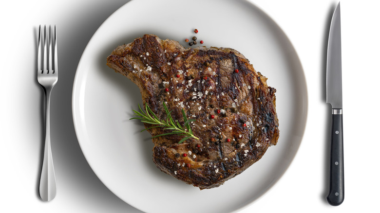 Cut of ribeye on a white plate with fork and knife next to it