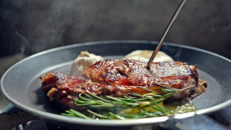 Piercing steak in pan with thermometer