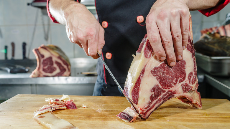 Person cutting ribeye steak in a kitchen with knife