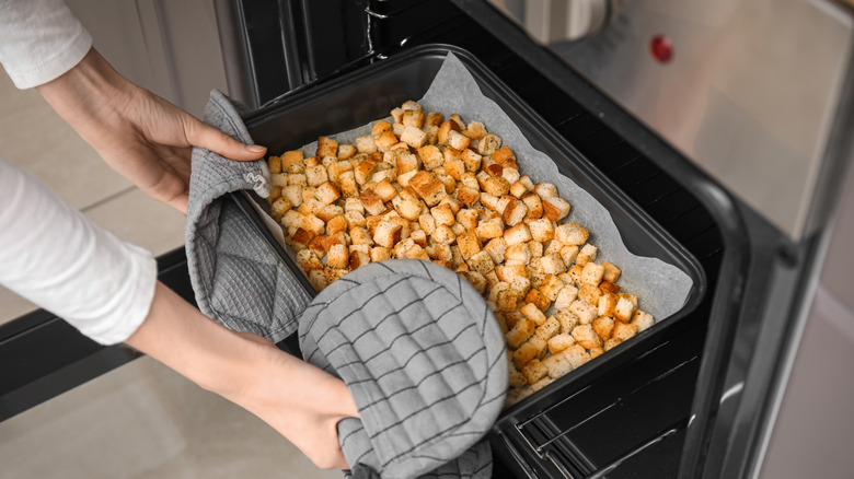 Person putting a baking sheet of cubes of bread in the oven
