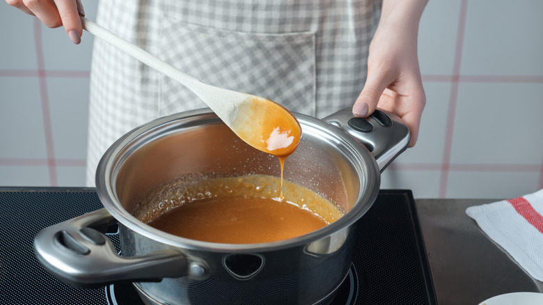 A hand holding a wooden spoon of caramel over a pot