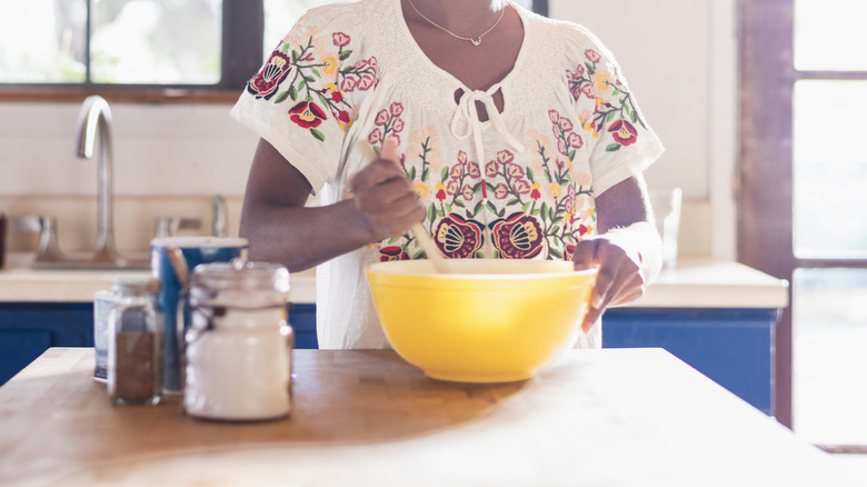 A person stirring yellow bowl with wooden spoon