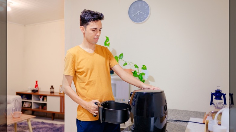 A person in a yellow shirt uses an air fryer in a cozy apartment.