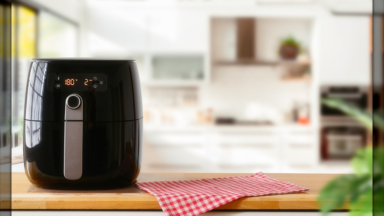 An air fryer sits on a kitchen counter top with a red and white checkered dish towel next to it.
