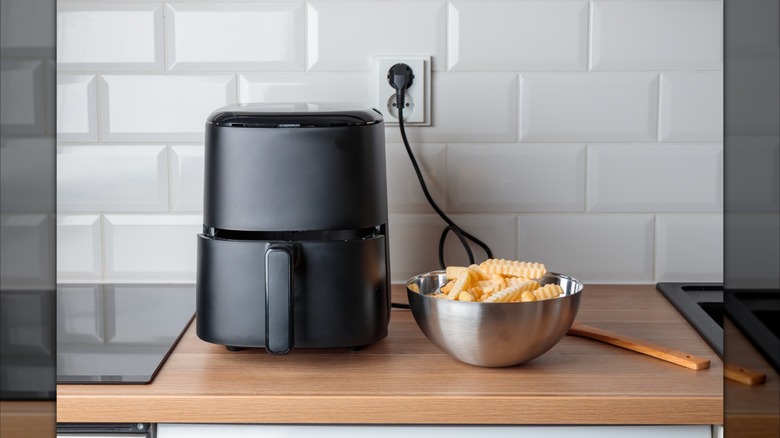 An airfryer and bowl of frozen fries sits on a counter top next to an electric stove top.