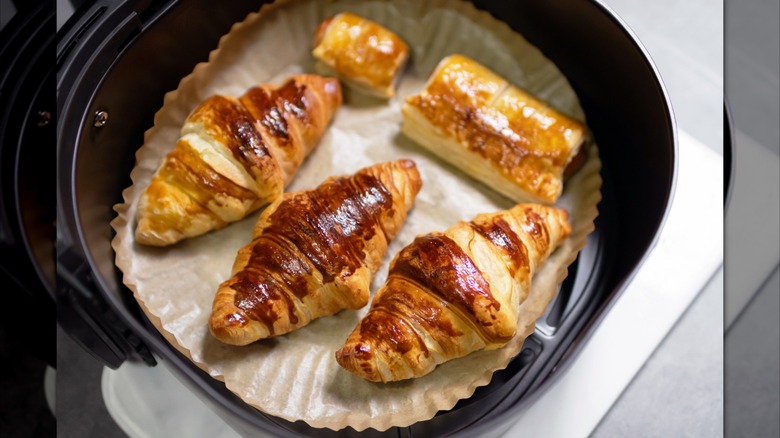 An air fryer basket filled with five pastries. The basket has a sheet of baking paper in the bottom.