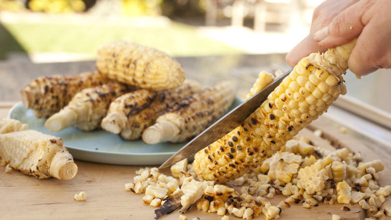 Person cutting corn kernels off of roasted corn